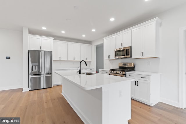 kitchen with a center island with sink, stainless steel appliances, white cabinetry, sink, and light hardwood / wood-style flooring