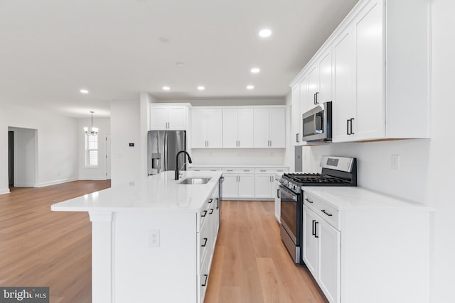 kitchen with white cabinets, light hardwood / wood-style floors, a kitchen island with sink, and appliances with stainless steel finishes