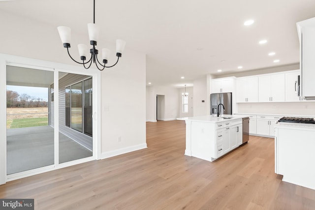 kitchen featuring a center island with sink, stainless steel appliances, white cabinetry, a notable chandelier, and light hardwood / wood-style floors