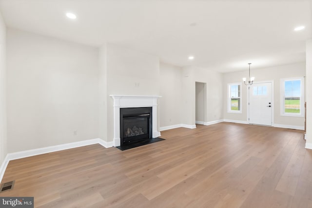 unfurnished living room featuring light wood-type flooring and an inviting chandelier