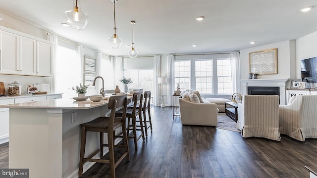 kitchen with dark wood-type flooring, hanging light fixtures, a center island with sink, and white cabinetry