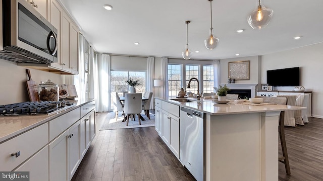 kitchen with pendant lighting, sink, dark hardwood / wood-style floors, appliances with stainless steel finishes, and a kitchen island with sink