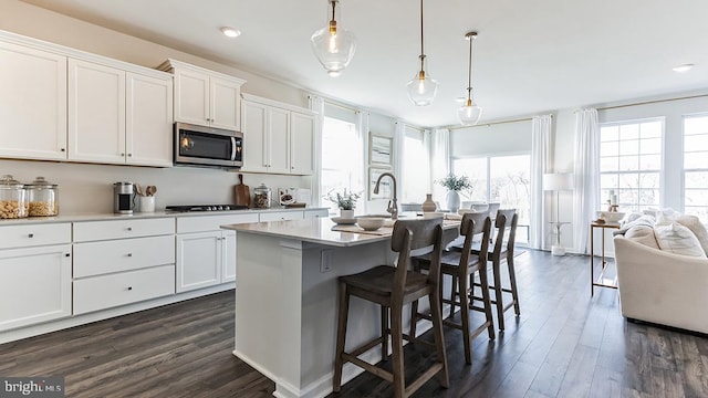 kitchen featuring decorative light fixtures, white cabinetry, a breakfast bar area, a center island with sink, and dark wood-type flooring