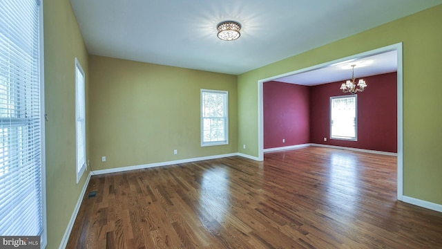 unfurnished room with a notable chandelier and dark wood-type flooring