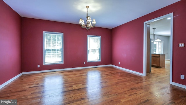 unfurnished room with a healthy amount of sunlight, an inviting chandelier, and hardwood / wood-style floors