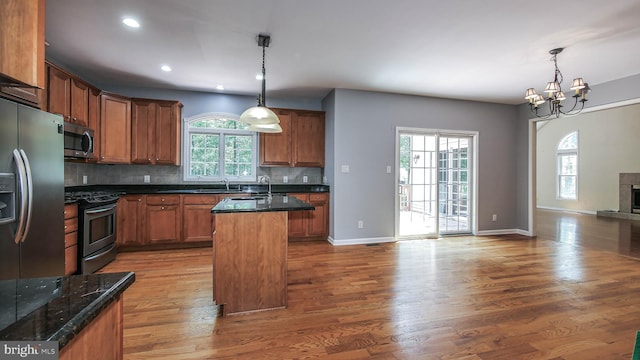 kitchen with wood-type flooring, a healthy amount of sunlight, appliances with stainless steel finishes, and an island with sink