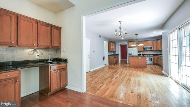 kitchen with tasteful backsplash, appliances with stainless steel finishes, pendant lighting, wood-type flooring, and sink