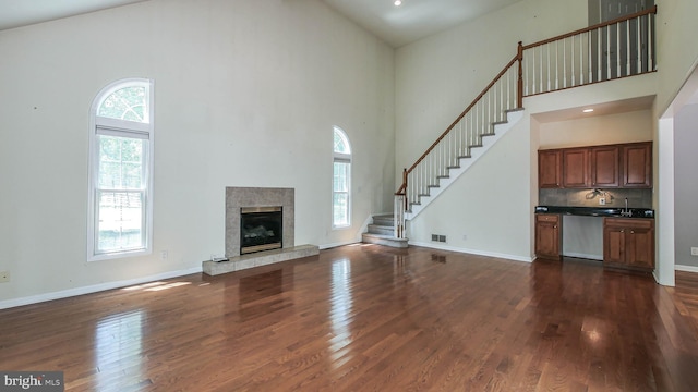 unfurnished living room featuring a tile fireplace, dark hardwood / wood-style floors, and a high ceiling