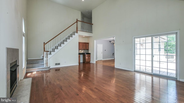 unfurnished living room with a premium fireplace, an inviting chandelier, wood-type flooring, and a towering ceiling