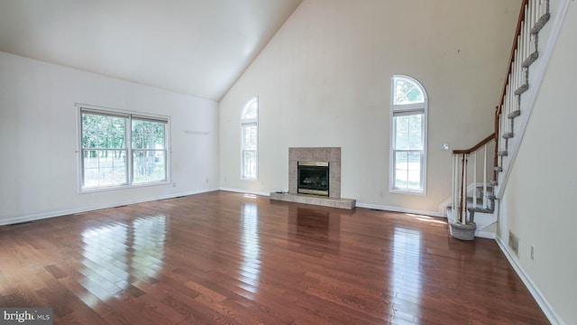 unfurnished living room with dark hardwood / wood-style floors, a tile fireplace, and high vaulted ceiling