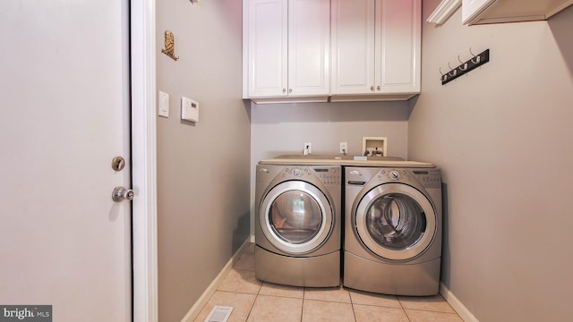 clothes washing area featuring cabinets, washer and dryer, and light tile patterned floors