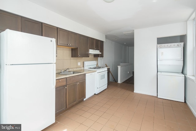 kitchen featuring stacked washer and dryer, tasteful backsplash, light tile patterned floors, white appliances, and sink