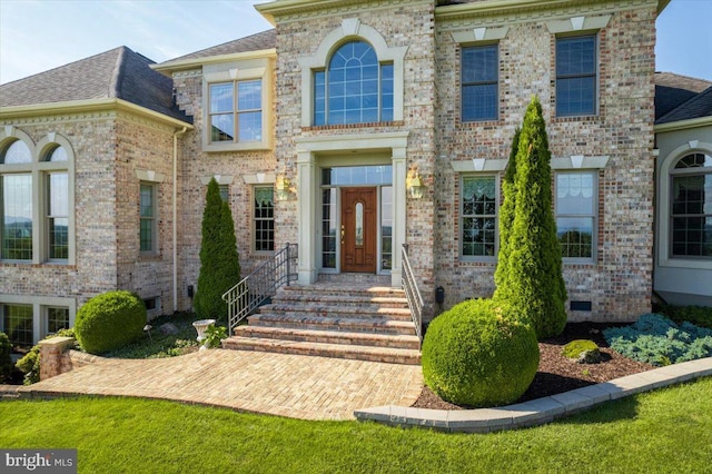 view of front facade with brick siding, crawl space, and a shingled roof