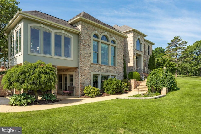 view of front of home with a front yard, a patio area, brick siding, and stucco siding