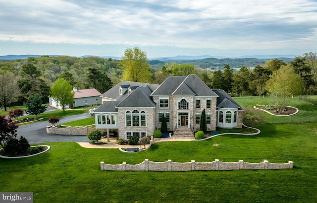 back of property with stone siding, a lawn, and a view of trees