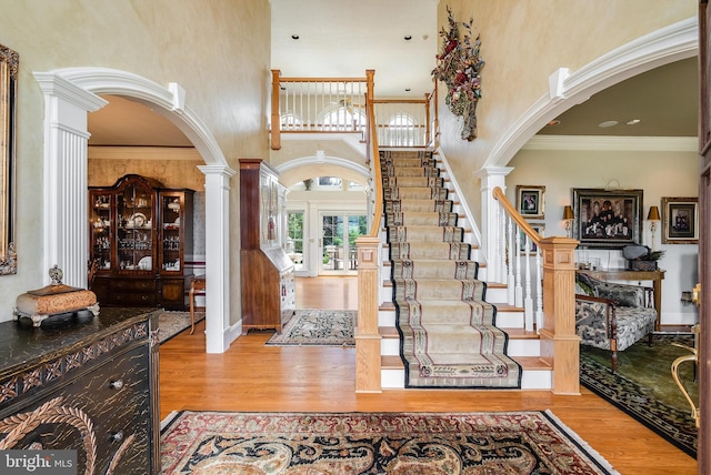 foyer with decorative columns, arched walkways, wood finished floors, and crown molding