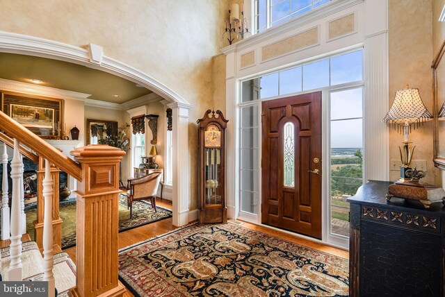 foyer entrance with light hardwood / wood-style flooring, a high ceiling, ornamental molding, and ornate columns