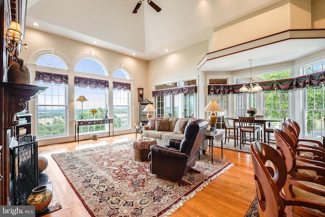 living room with a healthy amount of sunlight, a high ceiling, ceiling fan with notable chandelier, and light hardwood / wood-style flooring