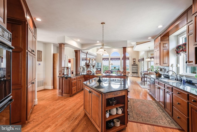 kitchen with dark stone countertops, a kitchen island, decorative columns, and light hardwood / wood-style floors