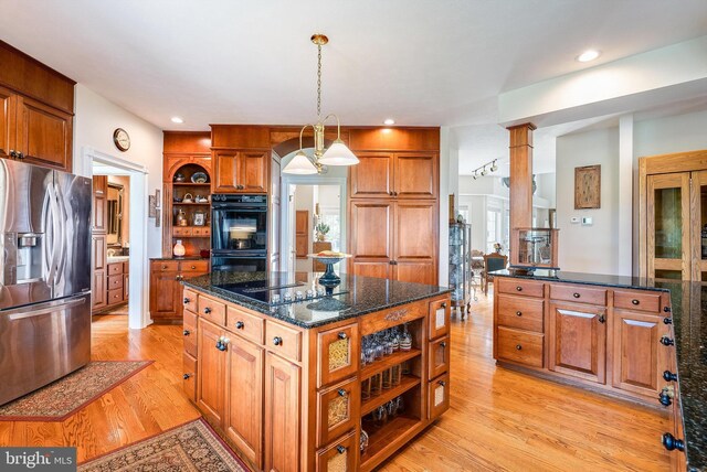 kitchen with dark stone countertops, decorative columns, black appliances, a kitchen island, and light hardwood / wood-style floors