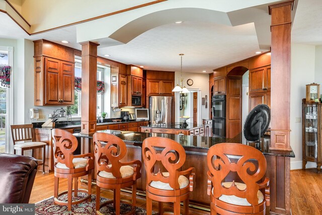 kitchen with a breakfast bar area, black appliances, decorative columns, a center island, and light wood-type flooring