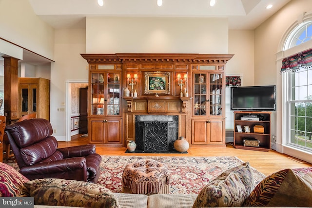 living room with decorative columns, light wood-style floors, a towering ceiling, and a fireplace