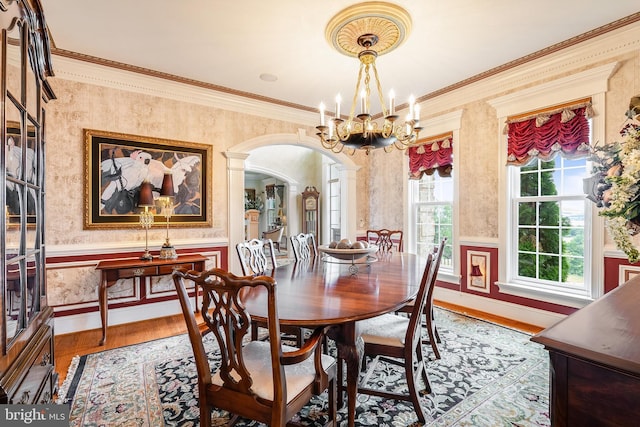 dining space featuring arched walkways, wood finished floors, crown molding, and wallpapered walls