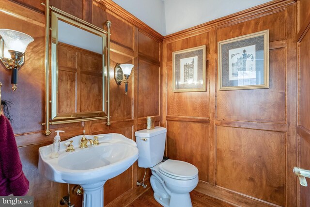 bathroom with toilet, sink, wooden walls, and hardwood / wood-style flooring