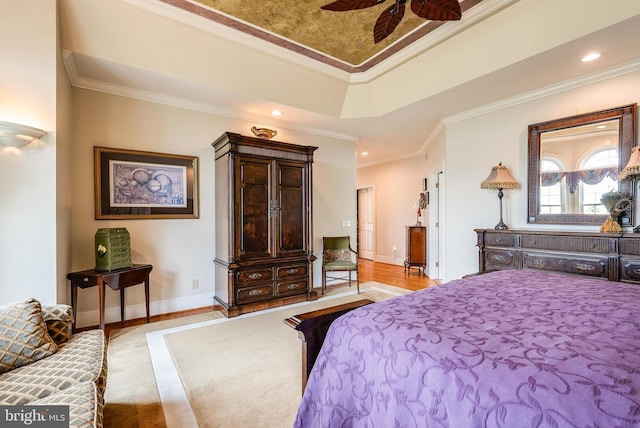 bedroom featuring light wood-type flooring, a tray ceiling, ceiling fan, and crown molding