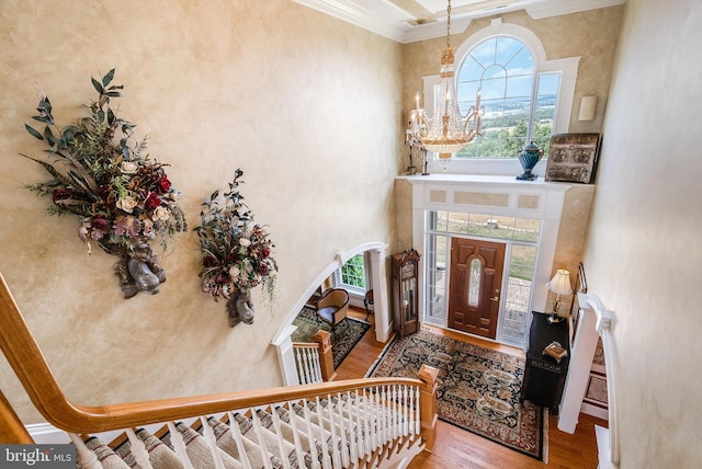 foyer entrance with a notable chandelier, ornamental molding, wood finished floors, arched walkways, and a towering ceiling