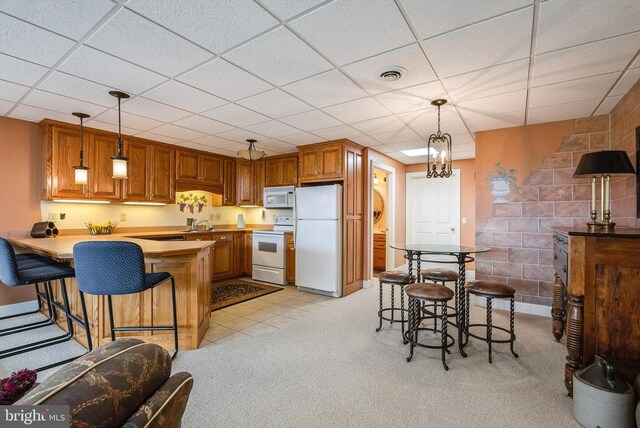 kitchen with white appliances, light colored carpet, a drop ceiling, and kitchen peninsula