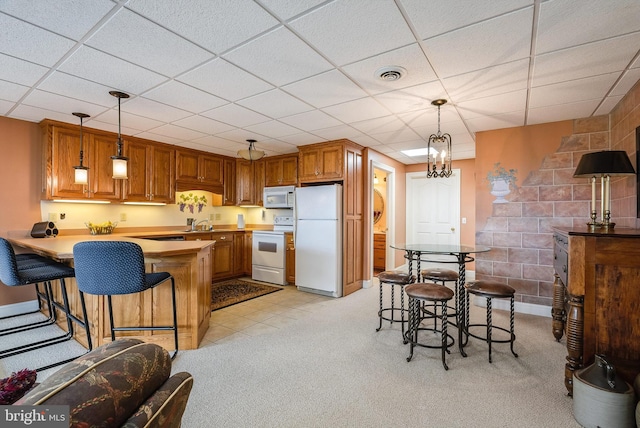 kitchen featuring visible vents, light carpet, a peninsula, brown cabinetry, and white appliances