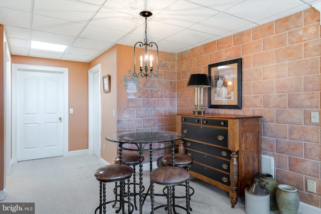 dining area with an accent wall, baseboards, a chandelier, a drop ceiling, and carpet floors