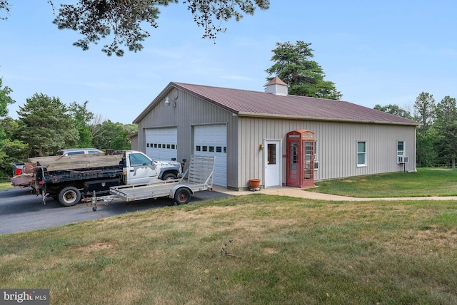 view of front of property with a detached garage, a front yard, a chimney, metal roof, and an outbuilding