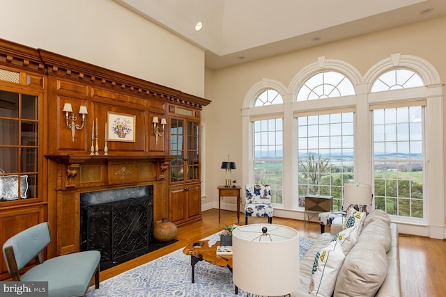 living area featuring a fireplace with flush hearth, recessed lighting, a high ceiling, and light wood-style floors