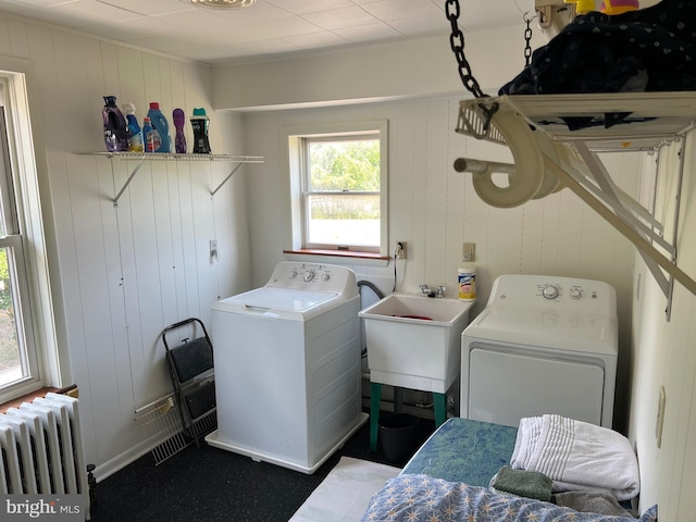 laundry area with washer and dryer, radiator, wood walls, and sink