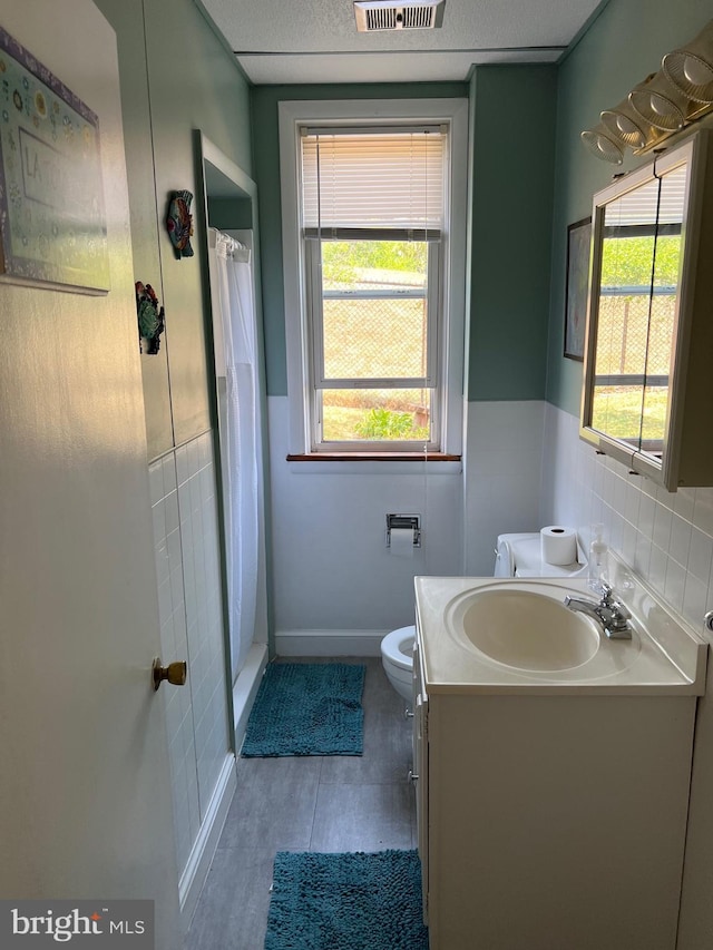 bathroom with toilet, a shower with curtain, tile walls, and vanity