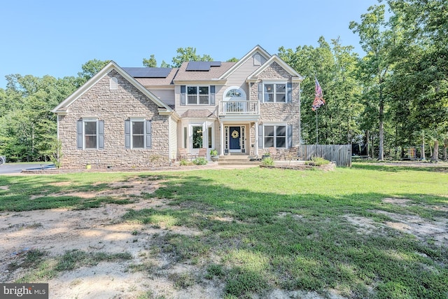 view of front of property with stone siding, a front yard, roof mounted solar panels, and a balcony