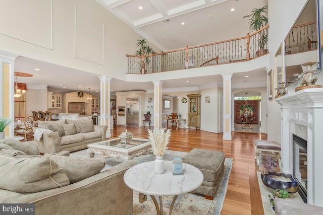 living room with a premium fireplace, ornate columns, light hardwood / wood-style floors, and coffered ceiling