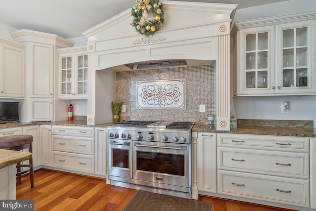 kitchen with range with two ovens, dark stone counters, light hardwood / wood-style flooring, and tasteful backsplash