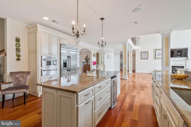 kitchen featuring light stone counters, a kitchen island, cream cabinets, stainless steel appliances, and light hardwood / wood-style floors