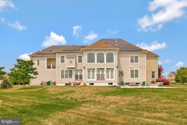 rear view of property with a patio, a lawn, and solar panels