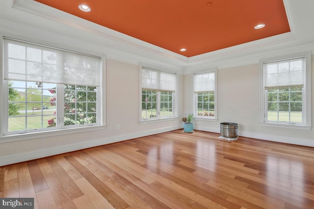 unfurnished living room with a raised ceiling, ornamental molding, and light wood-type flooring