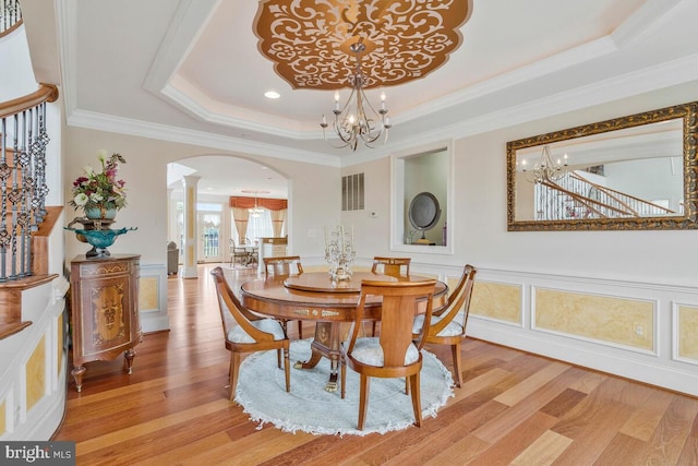 dining space featuring an inviting chandelier, a raised ceiling, light wood-type flooring, and ornamental molding