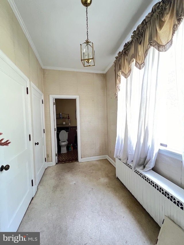 carpeted spare room with crown molding, radiator, and an inviting chandelier