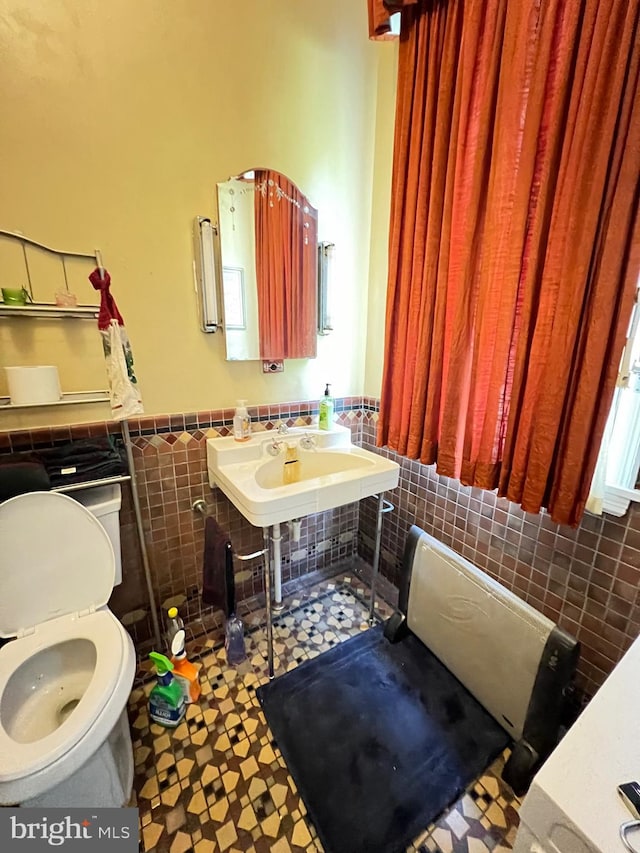 bathroom with toilet, sink, and tile walls