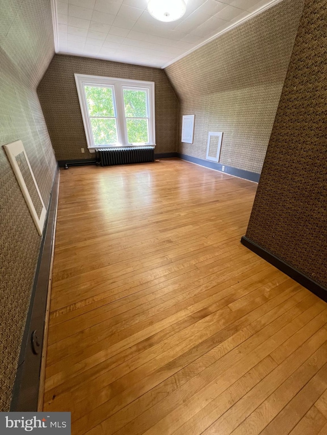 additional living space with vaulted ceiling, radiator heating unit, and light wood-type flooring