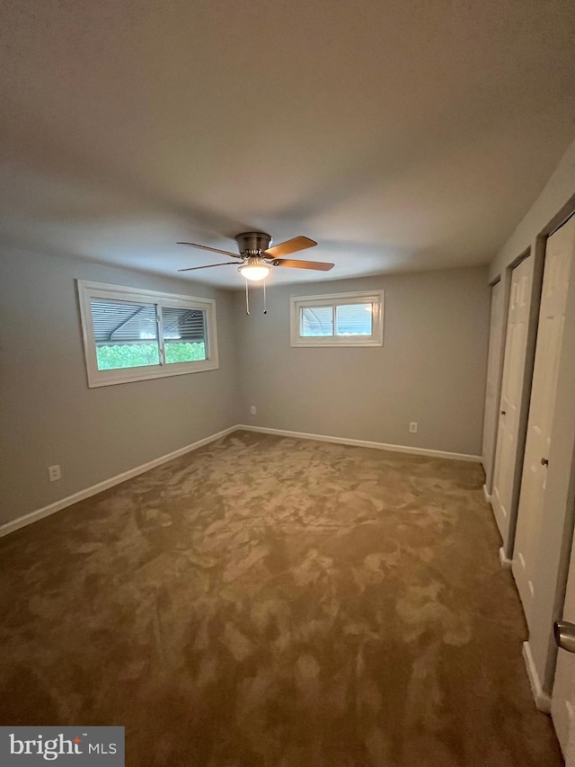 unfurnished bedroom with carpet floors, a ceiling fan, baseboards, and multiple closets