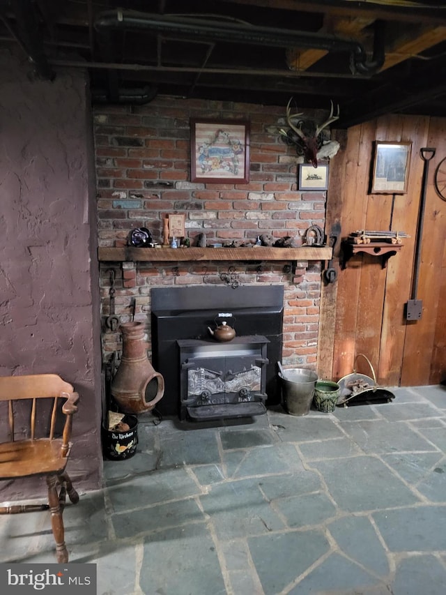 basement featuring brick wall, a wood stove, and wooden walls