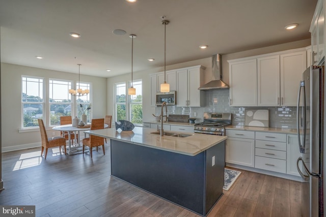 kitchen featuring stainless steel appliances, white cabinets, a sink, decorative light fixtures, and wall chimney exhaust hood